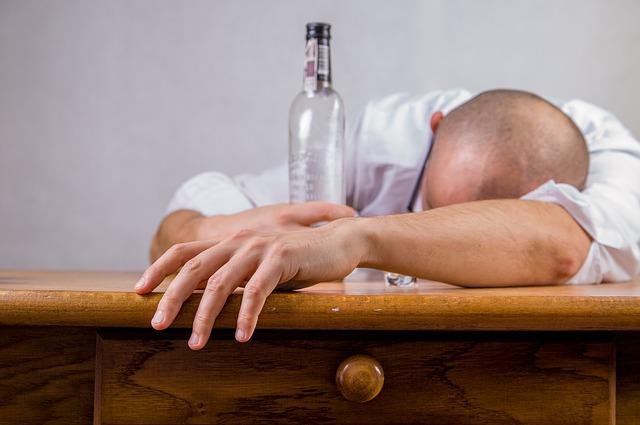 Hombre de resaca apoyado en una mesa con una botella vacía